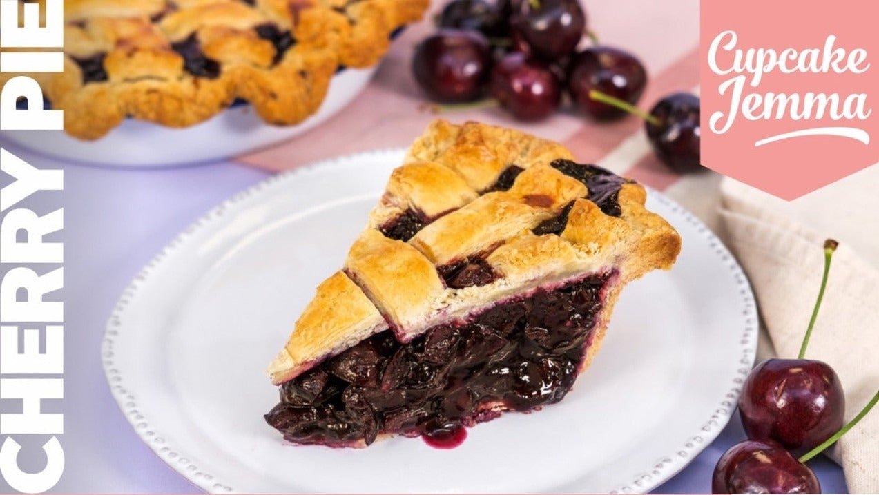 Slice of homemade cherry pie with lattice crust on a white plate alongside fresh cherries Cupcake Jemma recipe