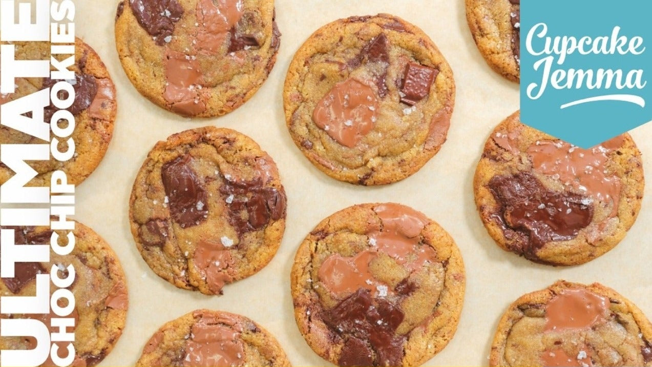 Close-up of freshly baked chocolate chip cookies with melted milk and dark chocolate chunks on parchment paper next to recipe ingredients list