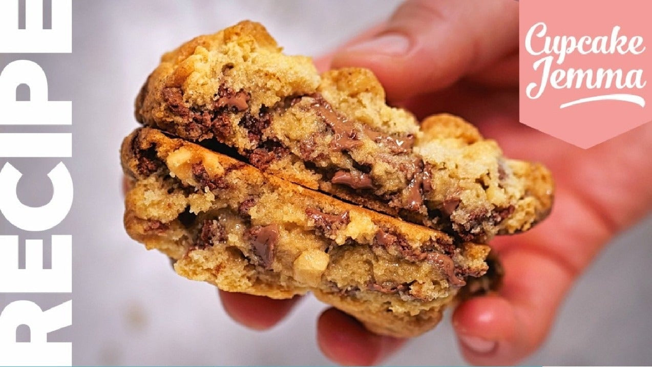 Close-up of a gooey chocolate chip New York cookie held between fingers with recipe details below by Cupcake Jemma