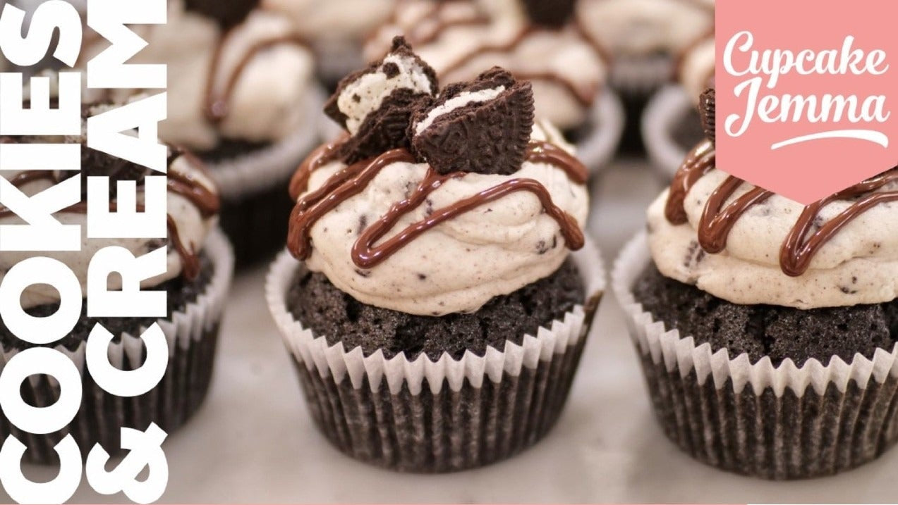 Close-up of rich cookies and cream cupcakes topped with frosting, crushed Oreos, and chocolate drizzle from Cupcake Jemma recipe.