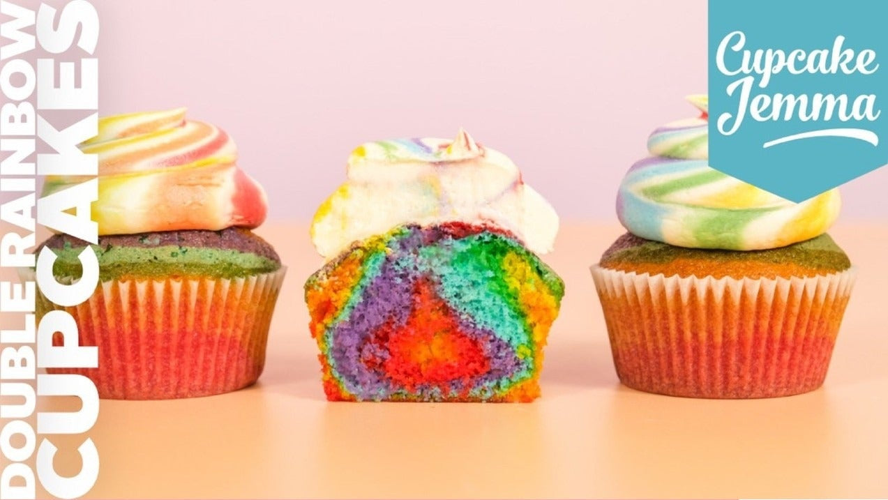 Three double rainbow cupcakes with colorful frosting and a cut one showing a vibrant rainbow interior from Cupcake Jemma recipe