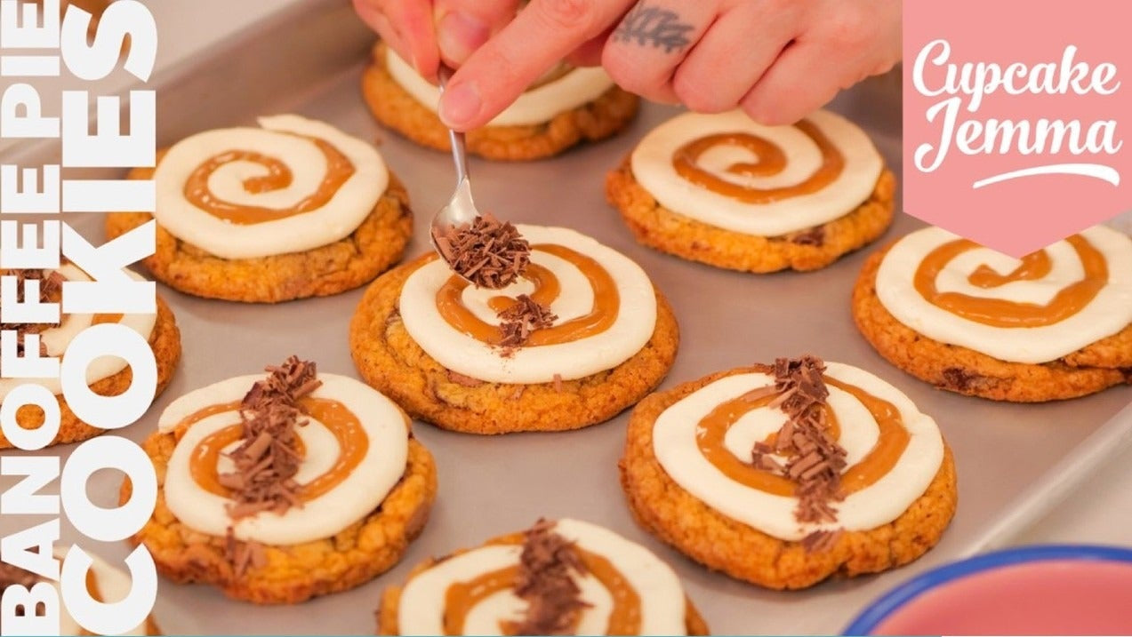 Hands decorating iced banoffee pie cookies with buttercream and chocolate shavings on a baking tray Cupcake Jemma recipe