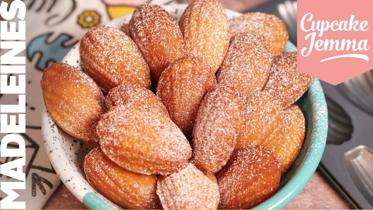 Bowl of lemon madeleines dusted with sugar alongside the Lemon Madeleines downloadable recipe by Cupcake Jemma