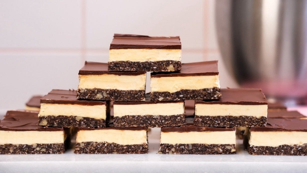 Stacked Nanaimo Bars with distinct layers of crumbly base, creamy custard center, and chocolate topping for a downloadable recipe.
