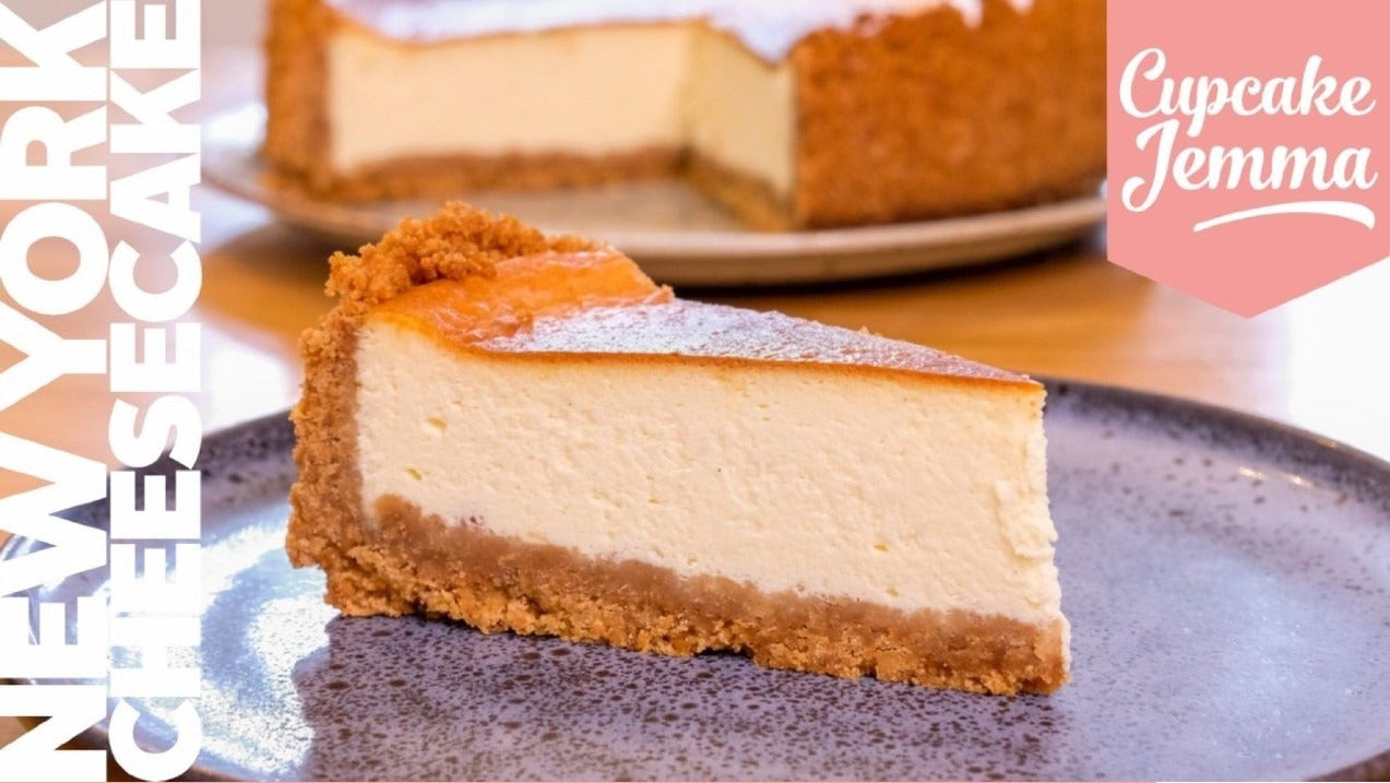 Slice of creamy New York Cheesecake on plate with recipe ingredients and Cupcake Jemma branding visible