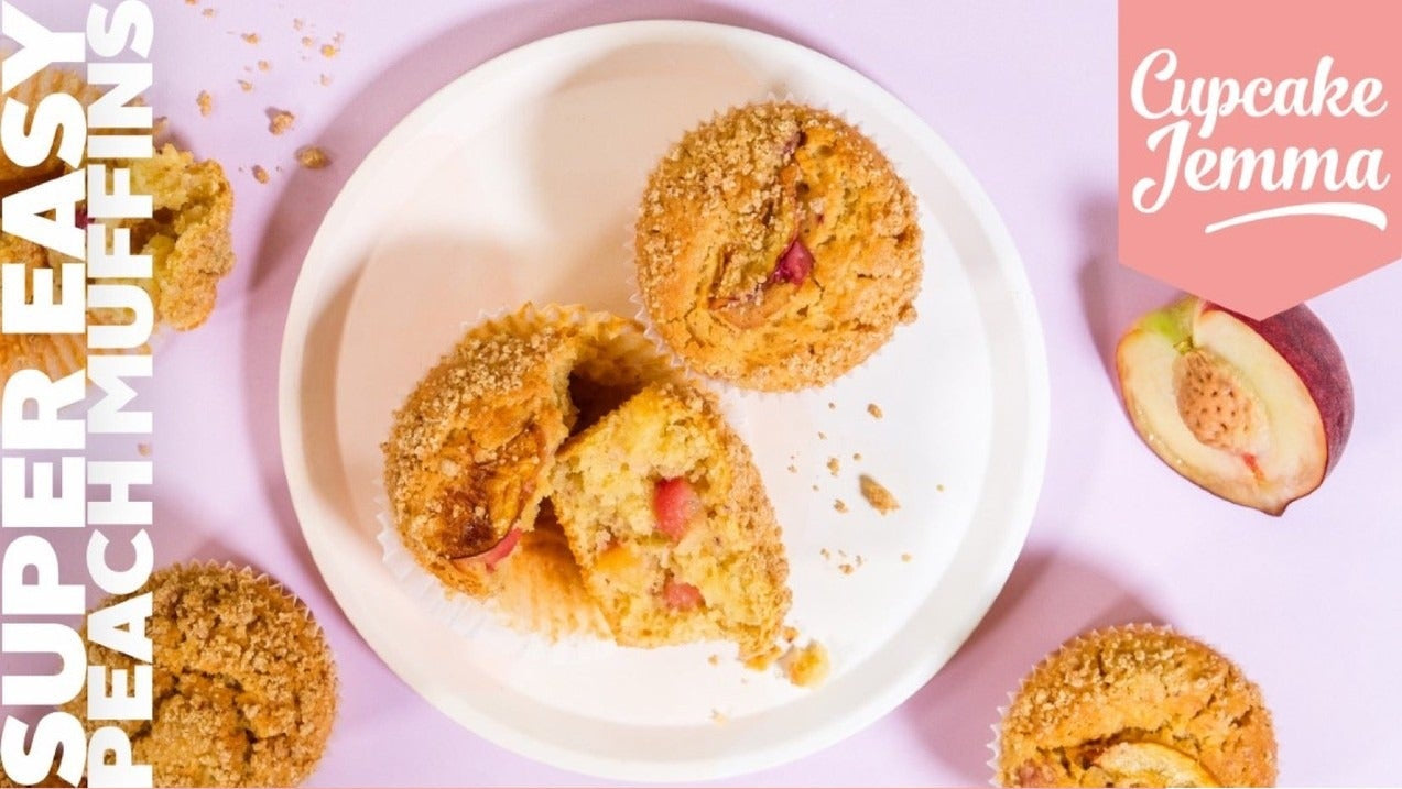 Peach muffins on a white plate with crumbs and recipe ingredients for Peach Muffins downloadable recipe by Cupcake Jemma