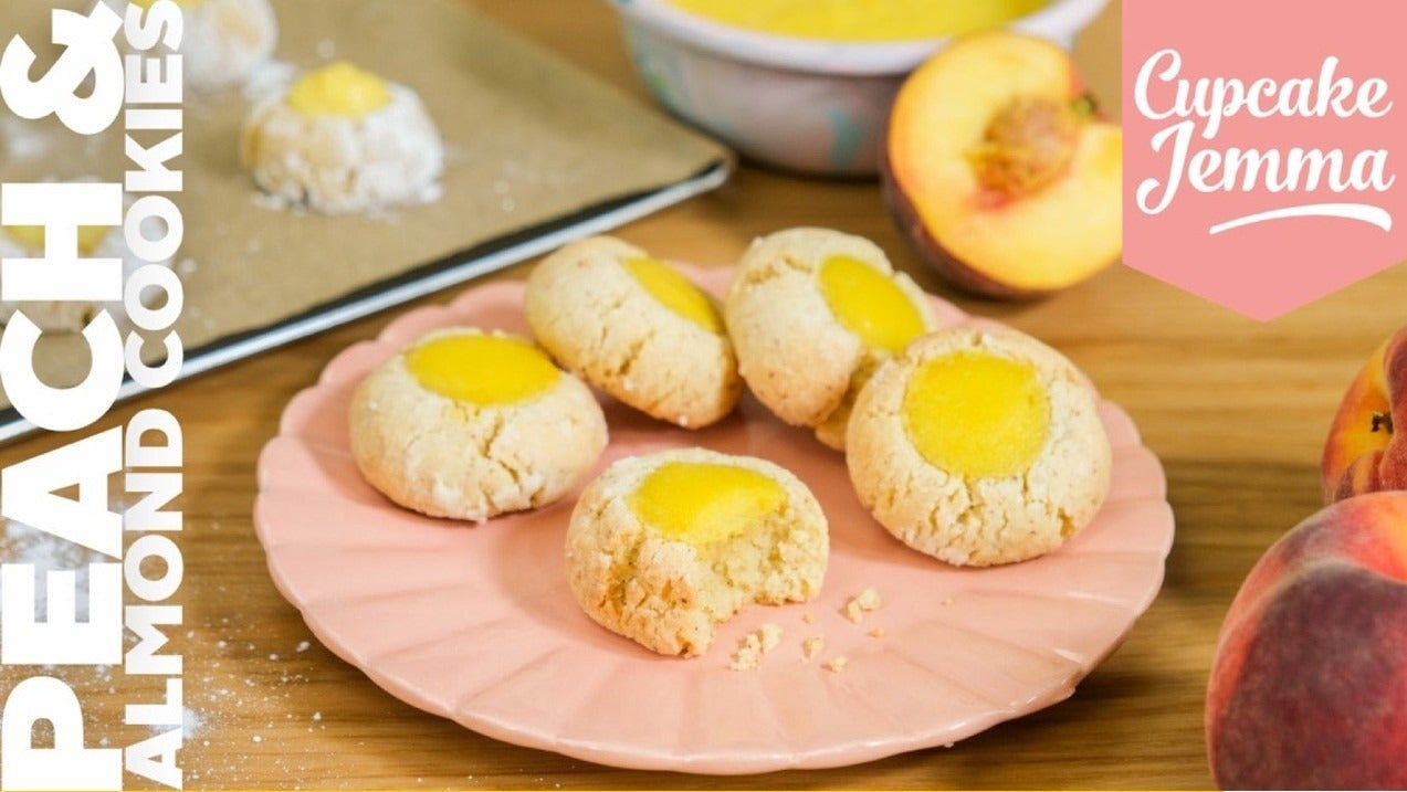 Peach & Almond Cookies on a pink plate with recipe ingredients and fresh peaches by Cupcake Jemma baking guide