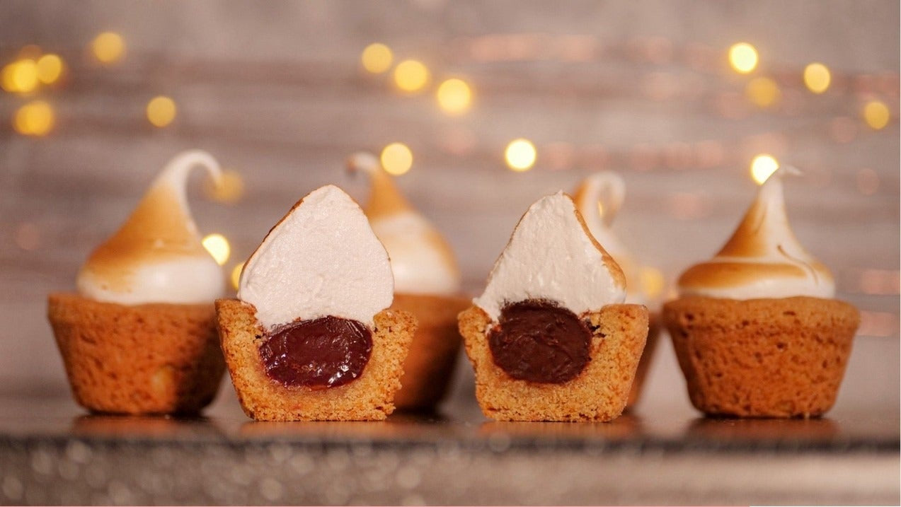 S'mores Cookie Cups with toasted meringue tops and chocolate filling, shown with recipe ingredients for baking.