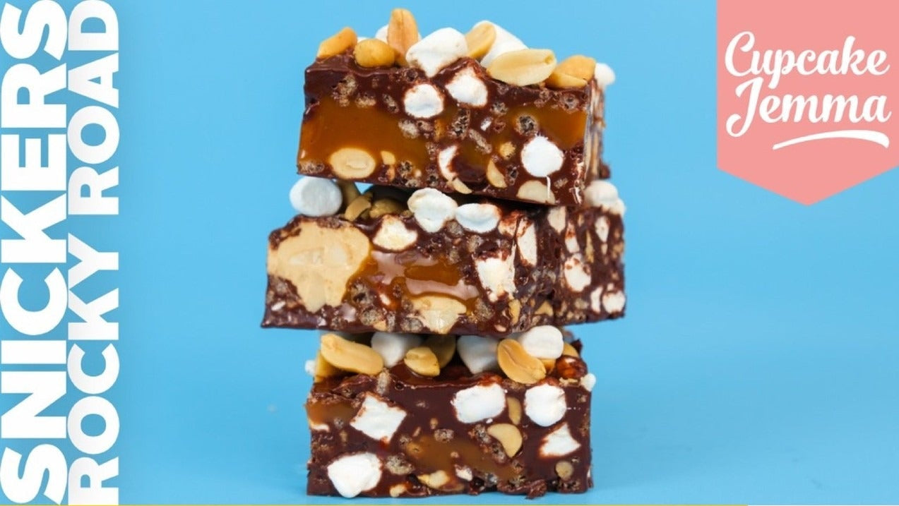 Three stacked Snickers Rocky Road bars showing peanuts, marshmallows, caramel, and chocolate chunks by Cupcake Jemma recipe.
