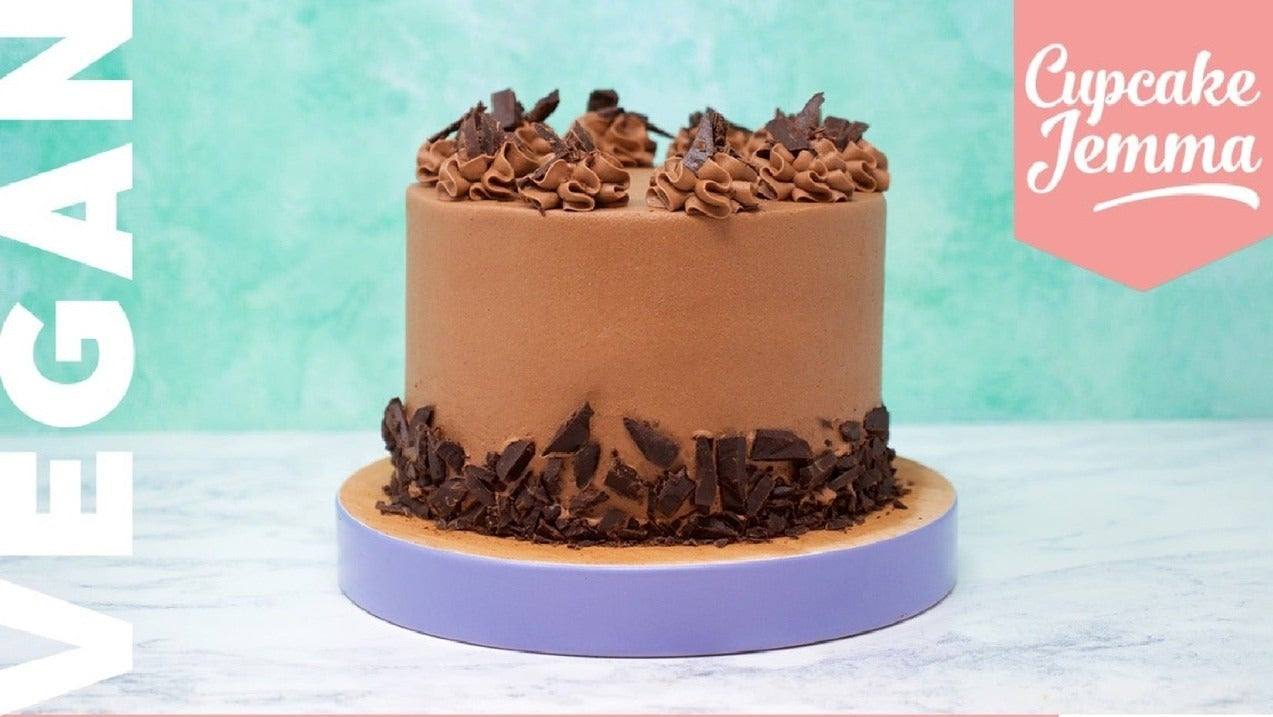 Round vegan chocolate cake with buttercream frosting and dark chocolate decorations on a purple stand by Cupcake Jemma