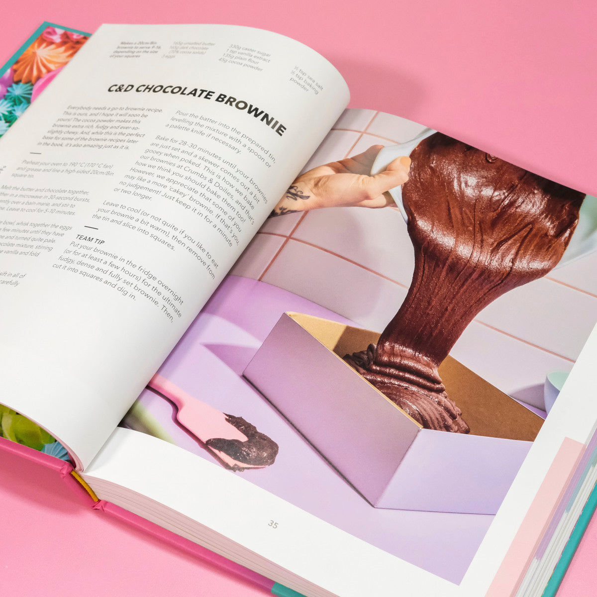 Open page of The Crumbs & Doilies Recipe Book showing a chocolate brownie recipe and pouring batter into a pan