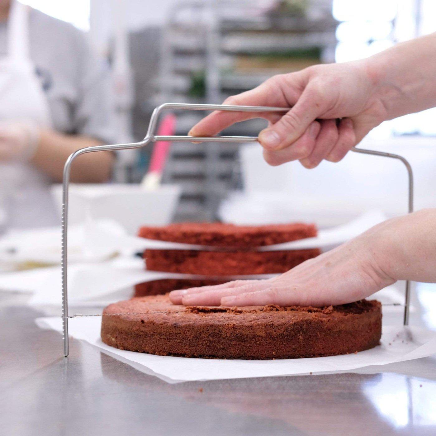 Woman using a Cake Leveller to slice an even layer from a chocolate sponge cake on a baking table